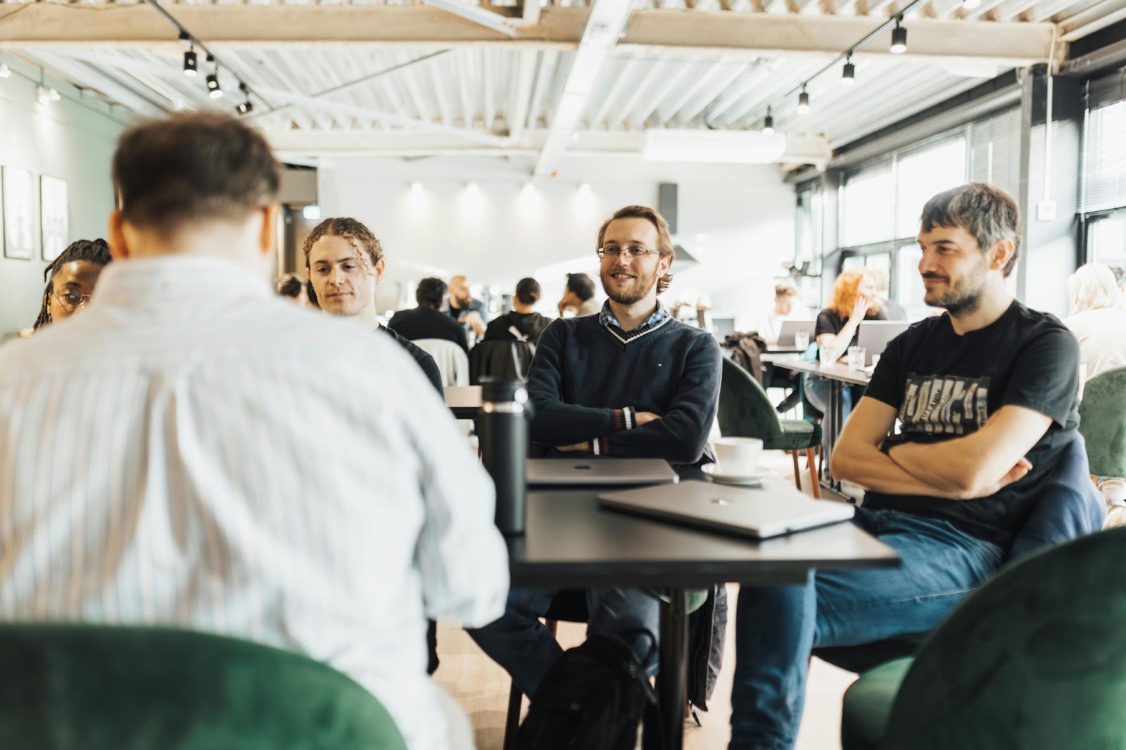 A group of colleagues engaged in a discussion around a table in a modern, well-lit office space.