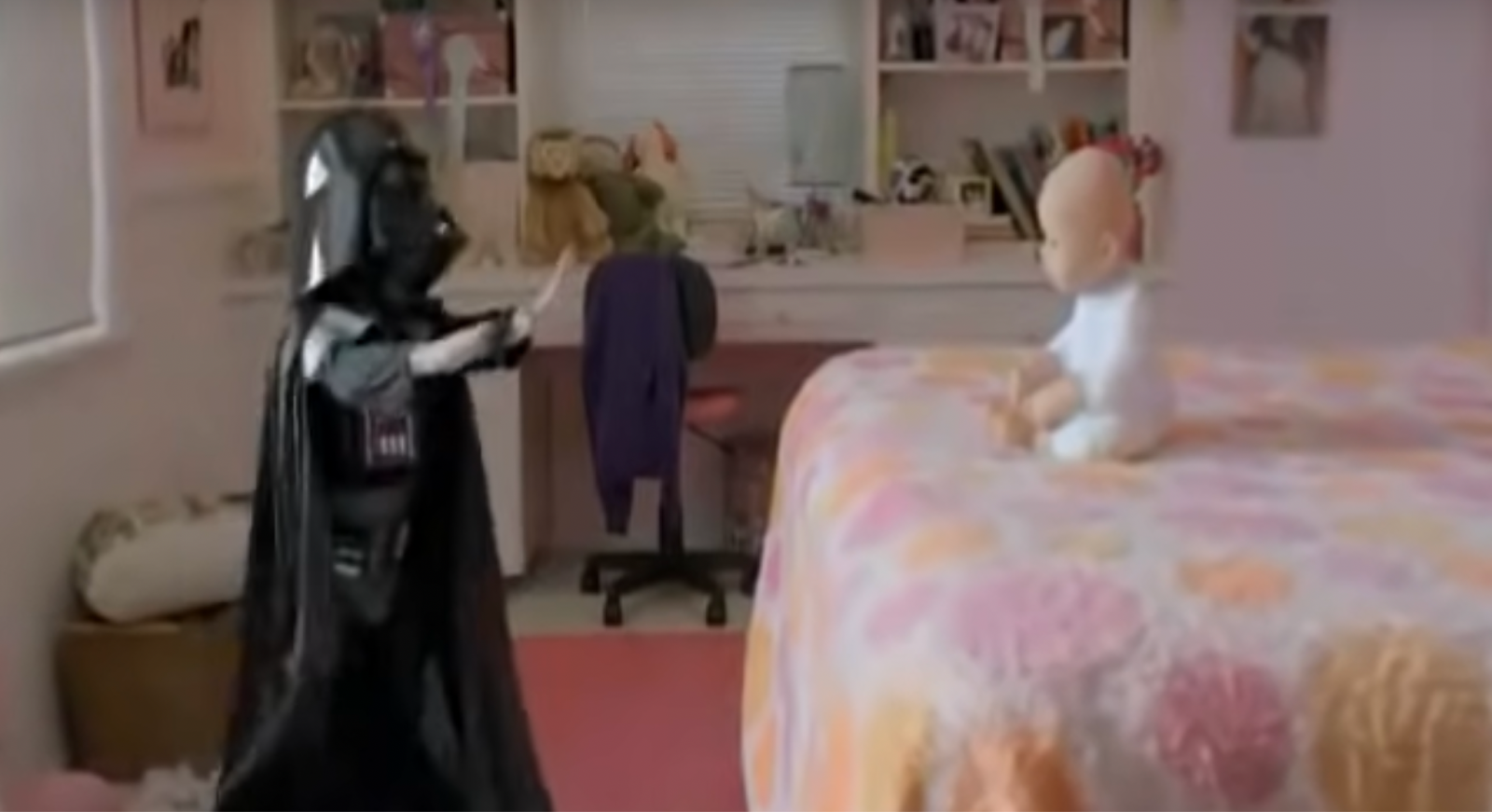 A child's bedroom with a realistic doll sitting on the flowered bedspread and a child dressed as Darth Vader standing on the floor nearby