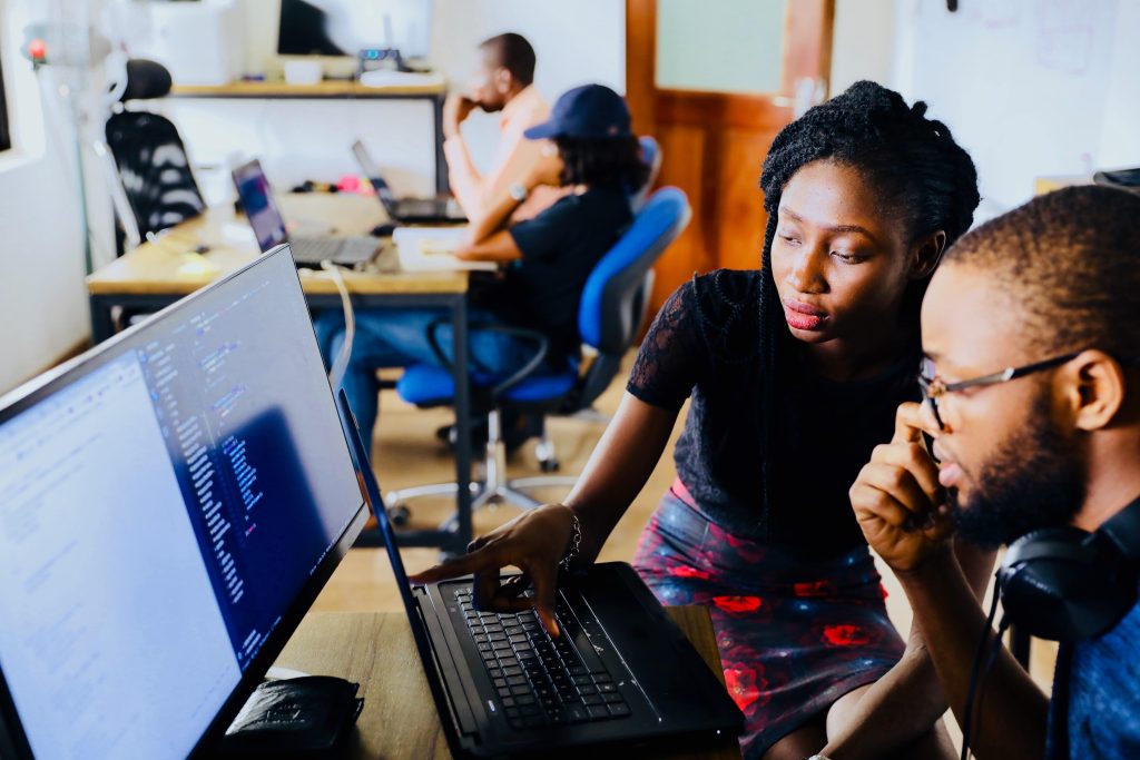 Two individuals collaborating on a computer in an office setting, engaged in work-related activities.