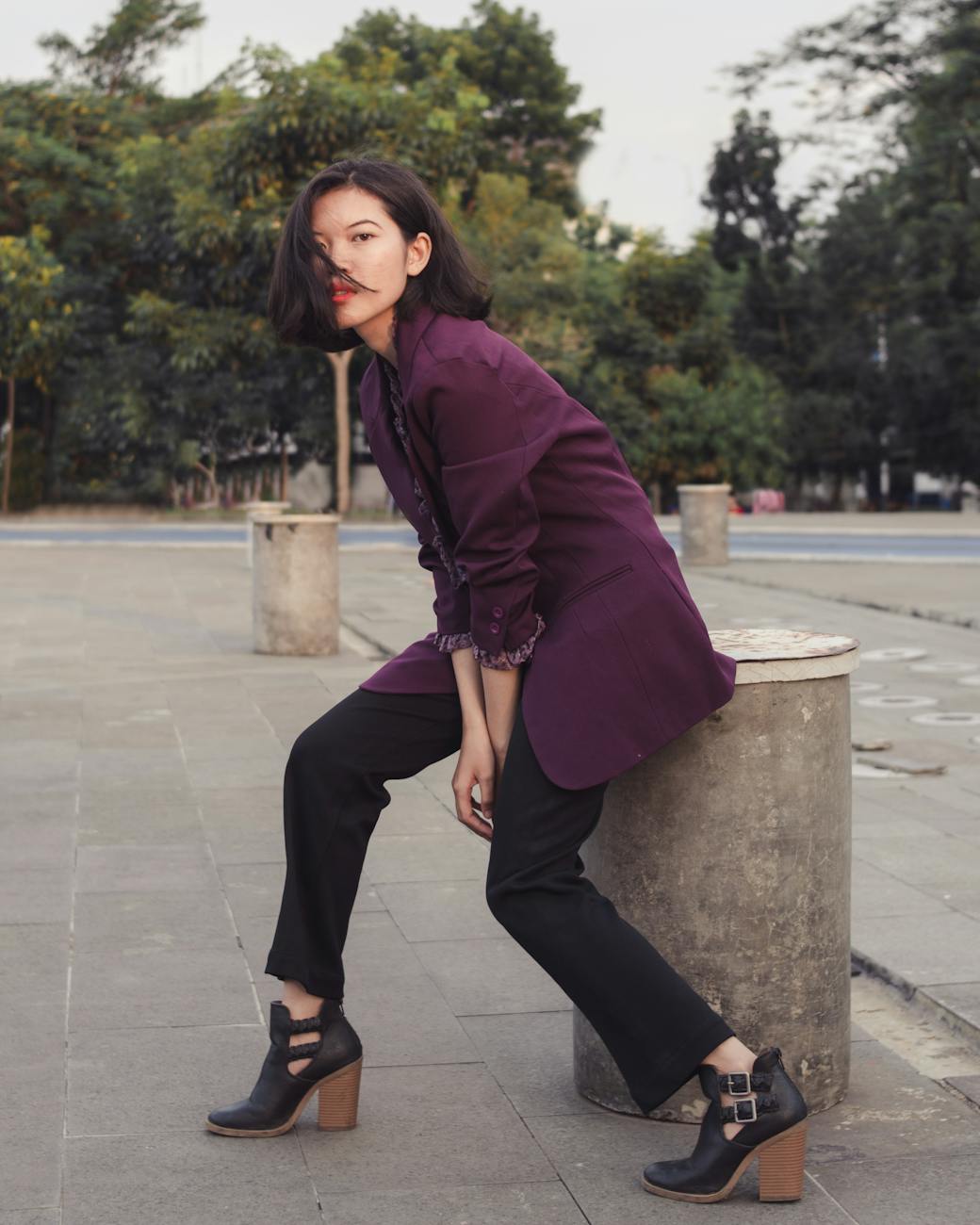 woman in maroon long sleeve blazer and black pants sitting on gray concrete