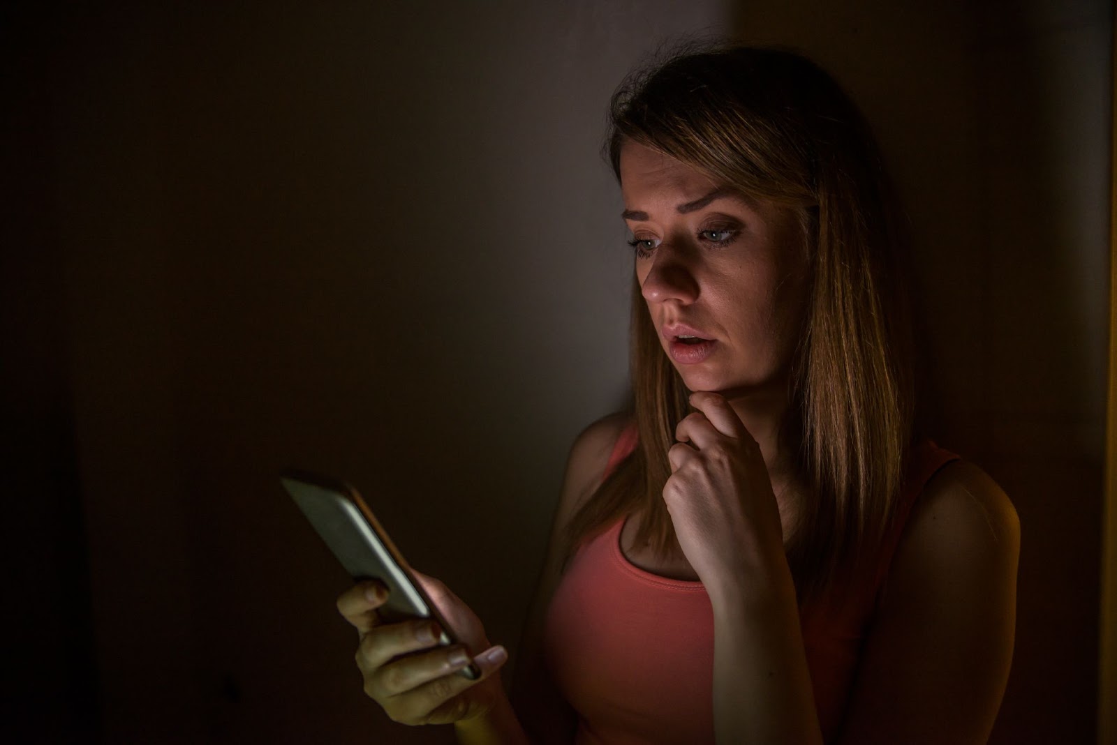 Worried woman looking at her phone in a dimly lit room