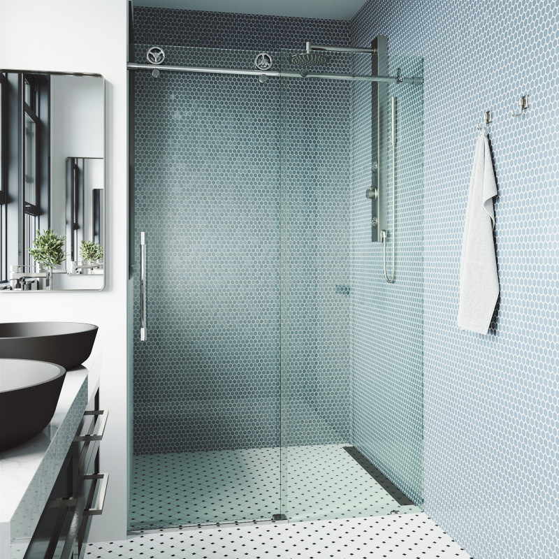 A glass shower door with a modern sliding motion on a polished metal frame, complementing the walls with stylish blue hexagonal mosaic tiles and a monochrome patterned floor. A towel of white fabric cascades down from a chrome hook, while at the front, black vessel double sinks are shown with a marble countertop. Keywords: glass shower door, blue mosaic tiles, modern bathroom design.