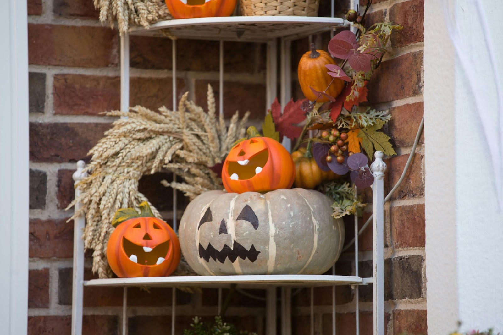 A white corner shelf featuring decorative jack-o-lanterns and fall foliage