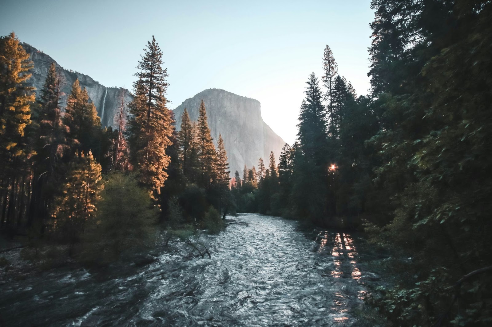 Sunset shot of a river in Yosemite National Park with mountains in the background and trees on either side.
