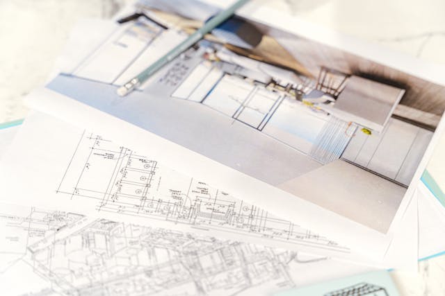 A close-up of a desk from an architectural firm showcases blueprints and a photo of a modern kitchen design.