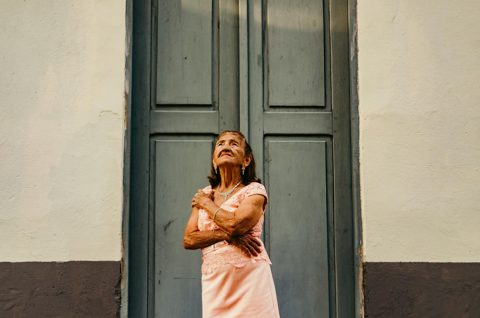 Elderly woman confidently poses in front of a rustic blue door, embodying grace and elegance.