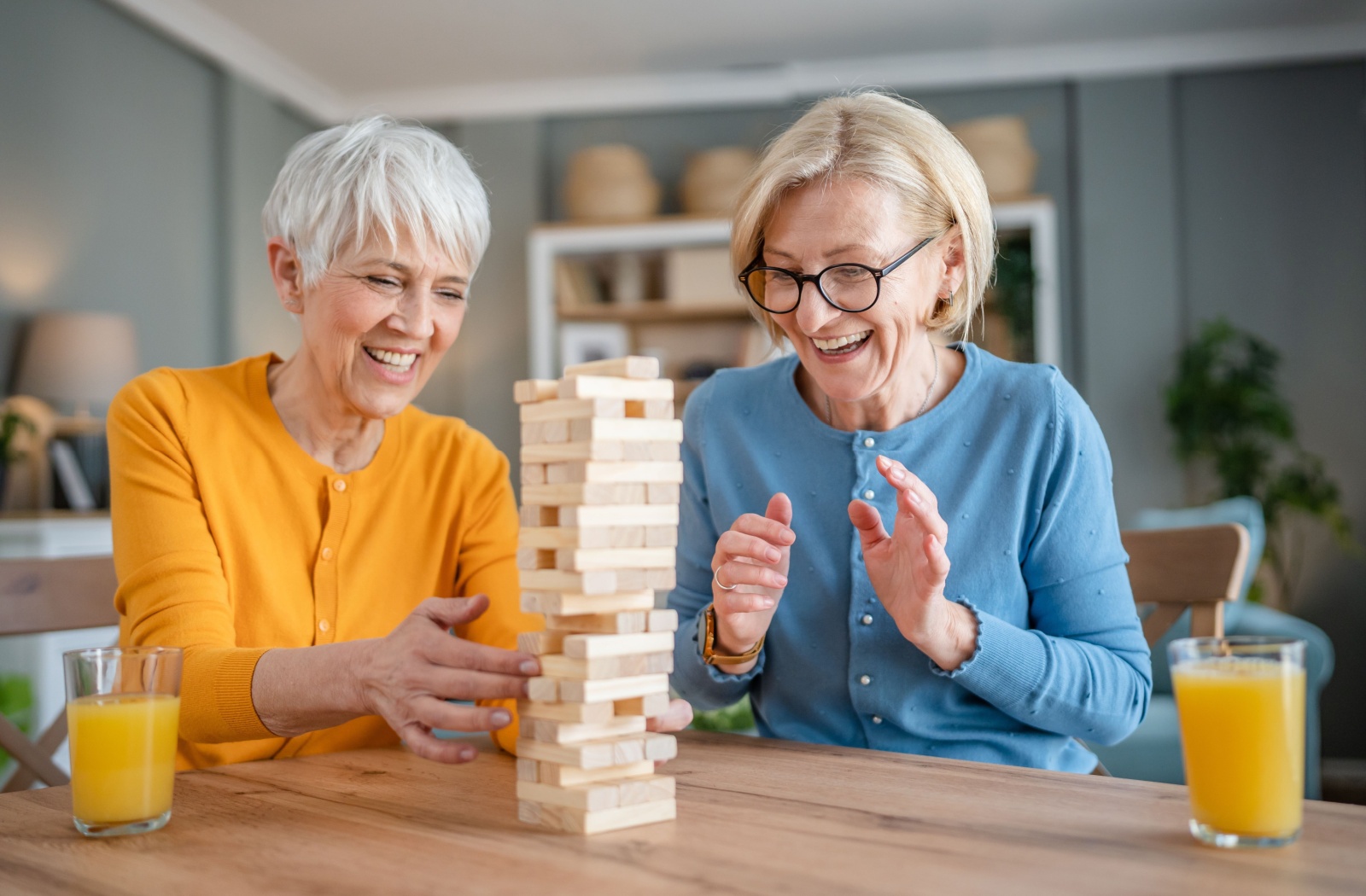 Two senior women laughing while engaging in a game of Jenga over breakfast.