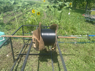 A spool of drip irrigation tape with a hoe through the middle, suspending the drip tape on a metal frame