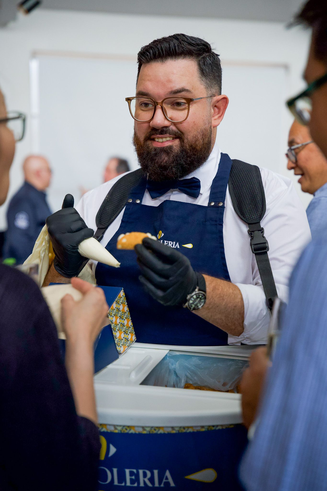 A person wearing an apron and gloves holding a pastry bagDescription automatically generated