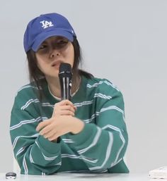 A picture Min Hee Jin wearing a navy blue cap and she's also wearing a green and white strip long sleeve dress holding a mic  