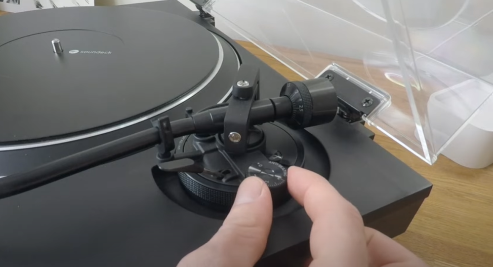 A person adjusting the anti-skate dial on a turntable.