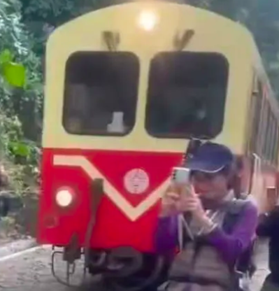 This contains an image of a woman  standing perilously close to the tracks, engrossed in taking photos.