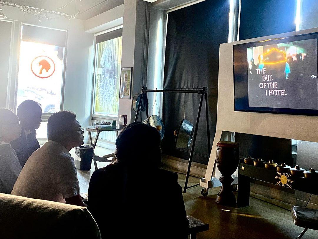 A group of people sitting in a room watching a television

Description automatically generated