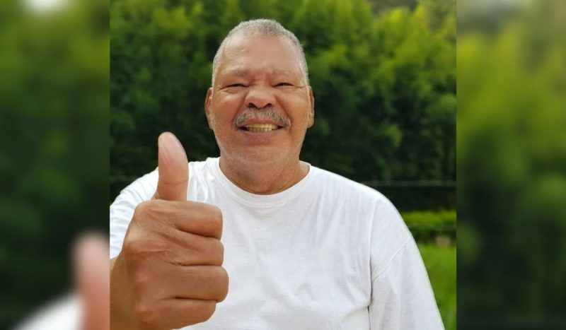 Maguila morreu aps ETC - homem negro, gordo, usando camiseta branca bsica, sorrindo e fazendo joinha com o dedo