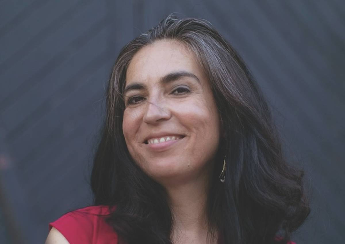 Tanya Talaga, an Anishinaabe woman, smiles in front of a dark background