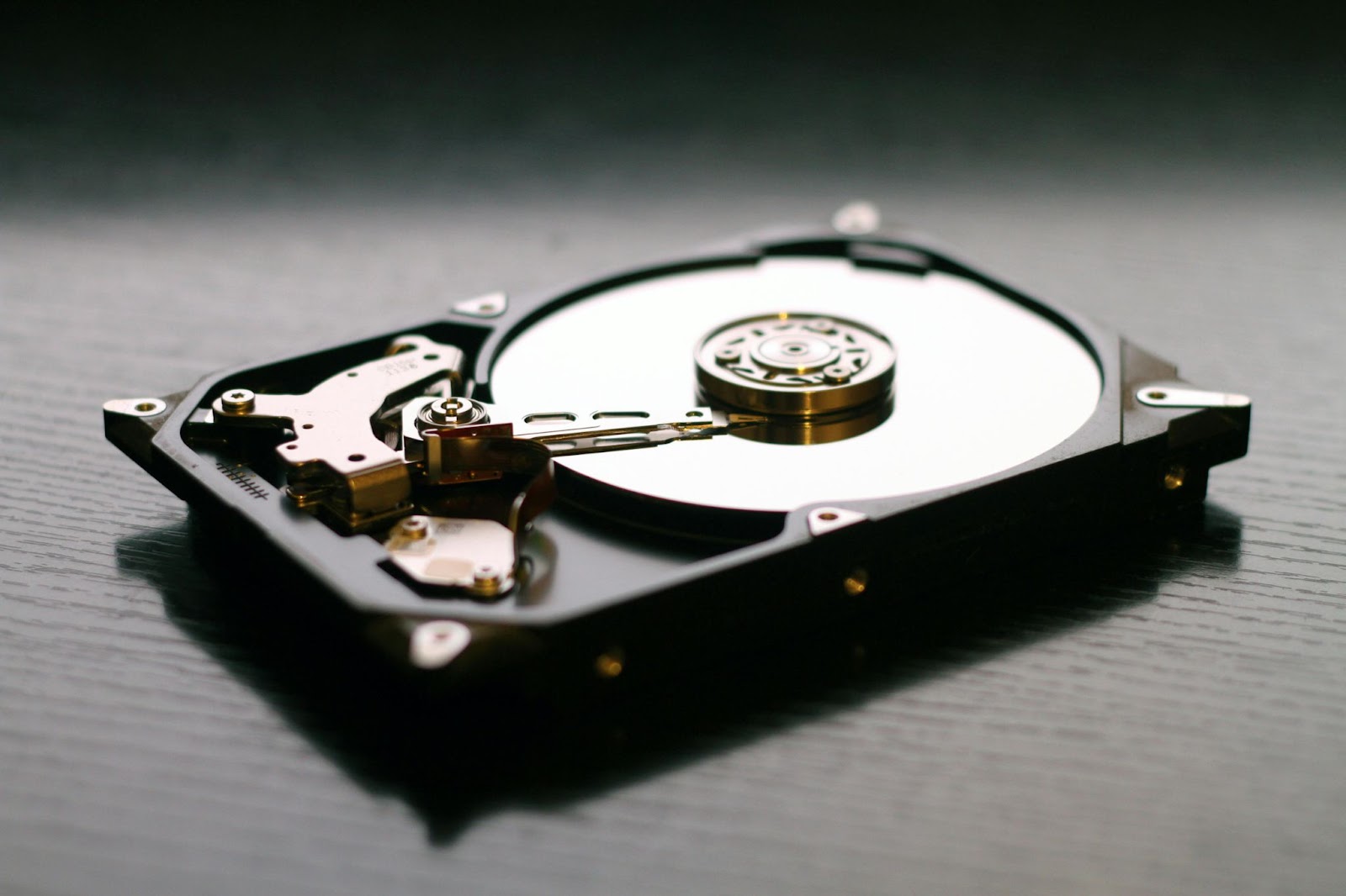 A close-up of an open hard drive, showing its internal components, including the read/write arm and the spinning disk platters, on a dark surface.