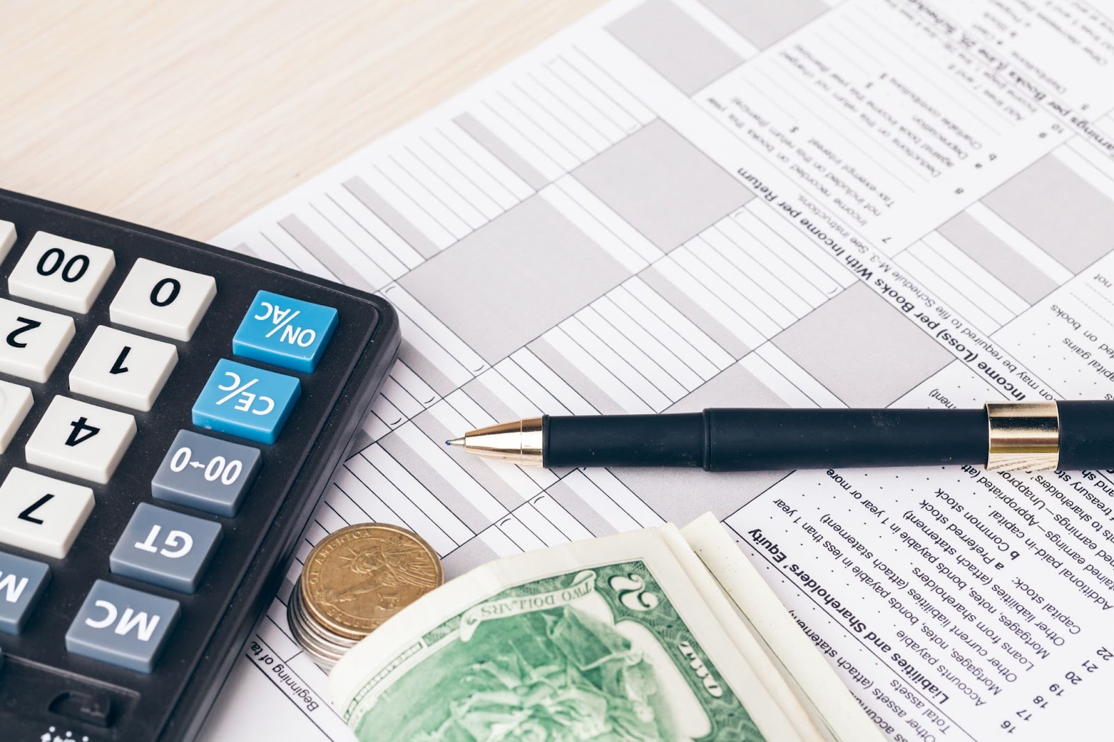 Tax form next to a calculator, pen, coins, and a wad of cash. 