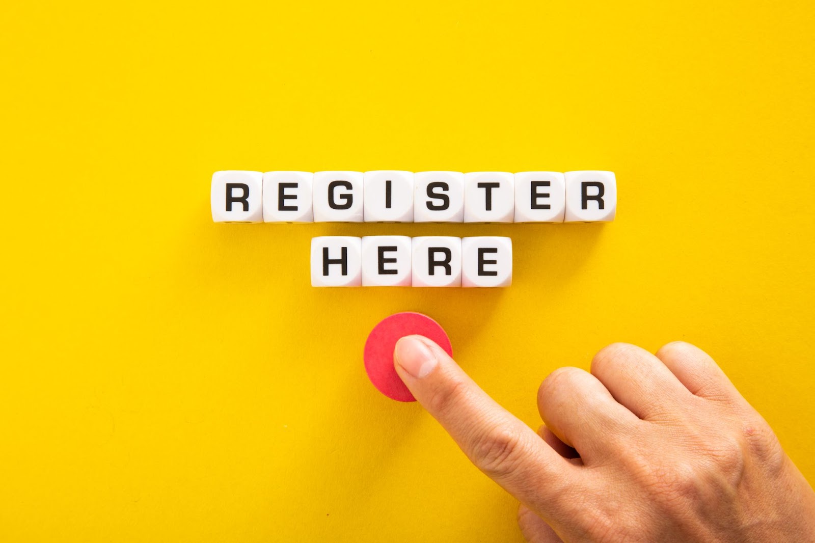 Words “register here” on dice with a person pushing a red button. 