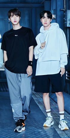 This contain an image of Jin and J-Hope standing next to each other in front of a blue wall and floor