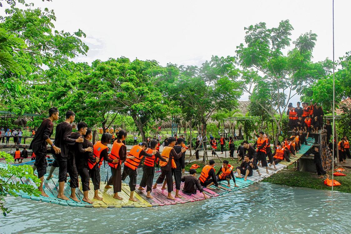 A group of people in orange vests on a surfboardDescription automatically generated