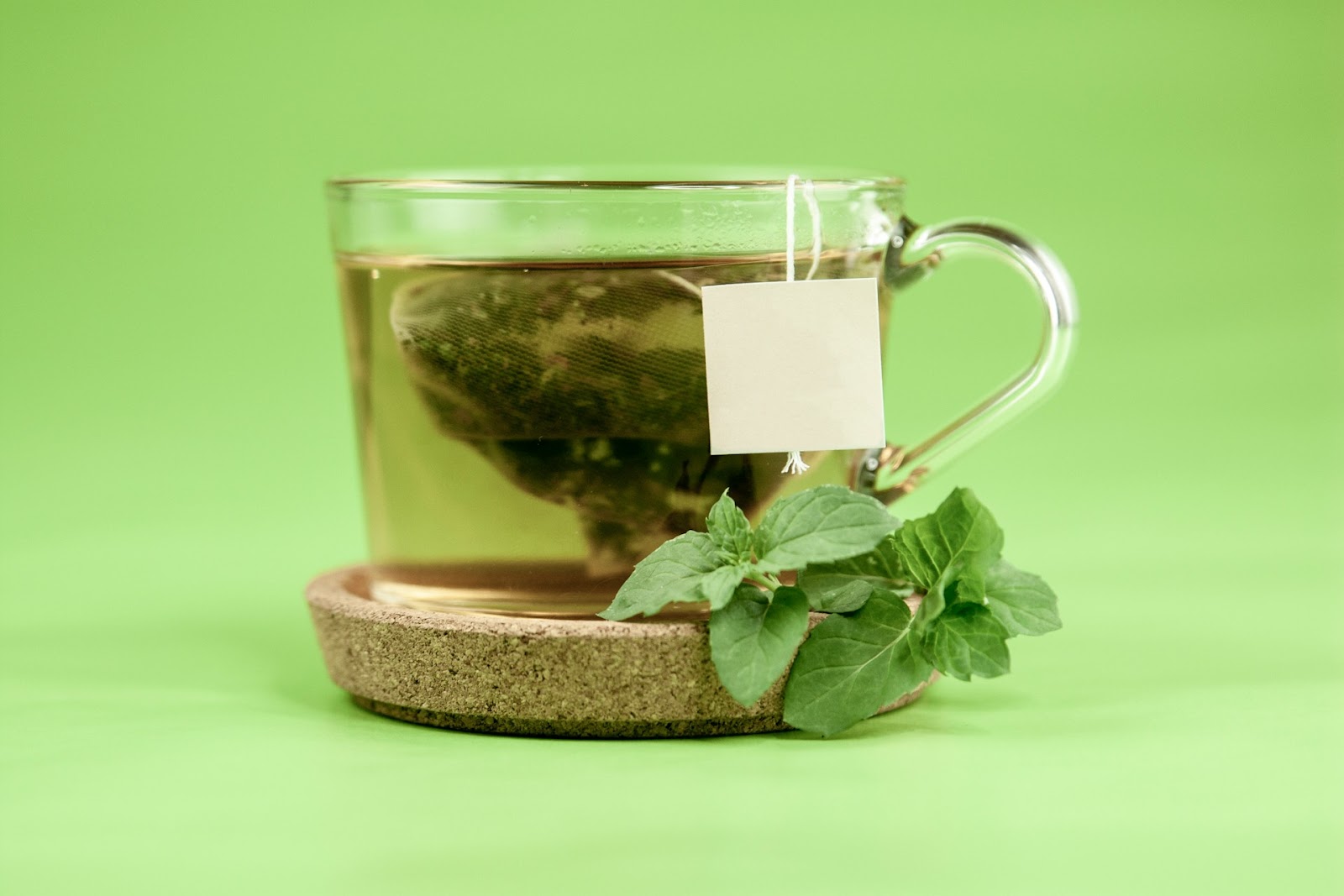 An aesthetic shot of a green tea bag in a clear cup with a green background