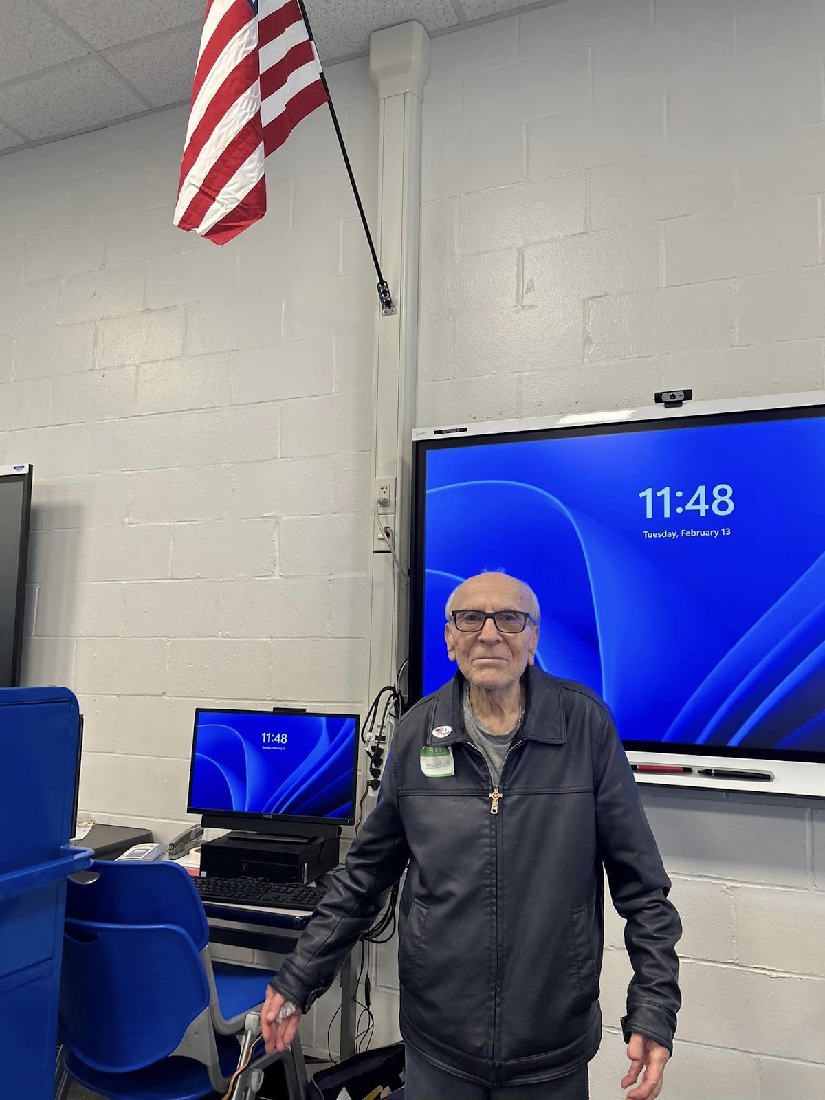 A senior citizen standing in front of a large screen monitor