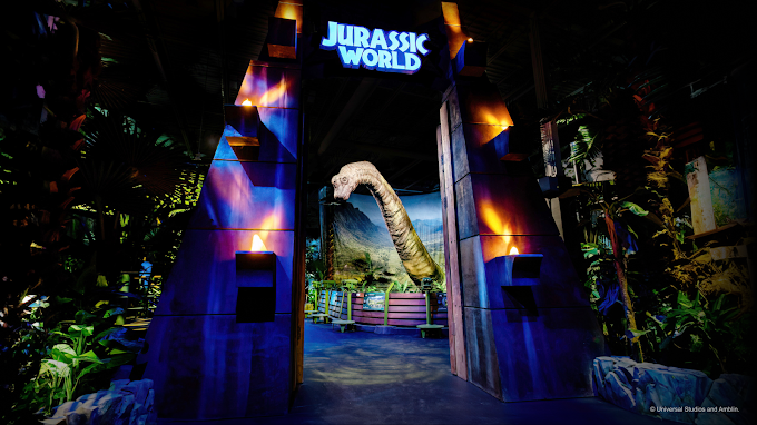 Entrance to Jurassic World: The Exhibition at The Trafford Centre, featuring the iconic Jurassic World gates and life-sized dinosaur displays