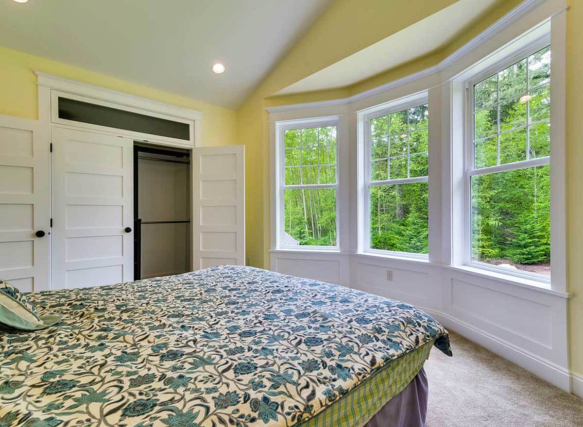 Another bedroom with yellow walls, a bay window, carpet flooring, and a walk-in closet.