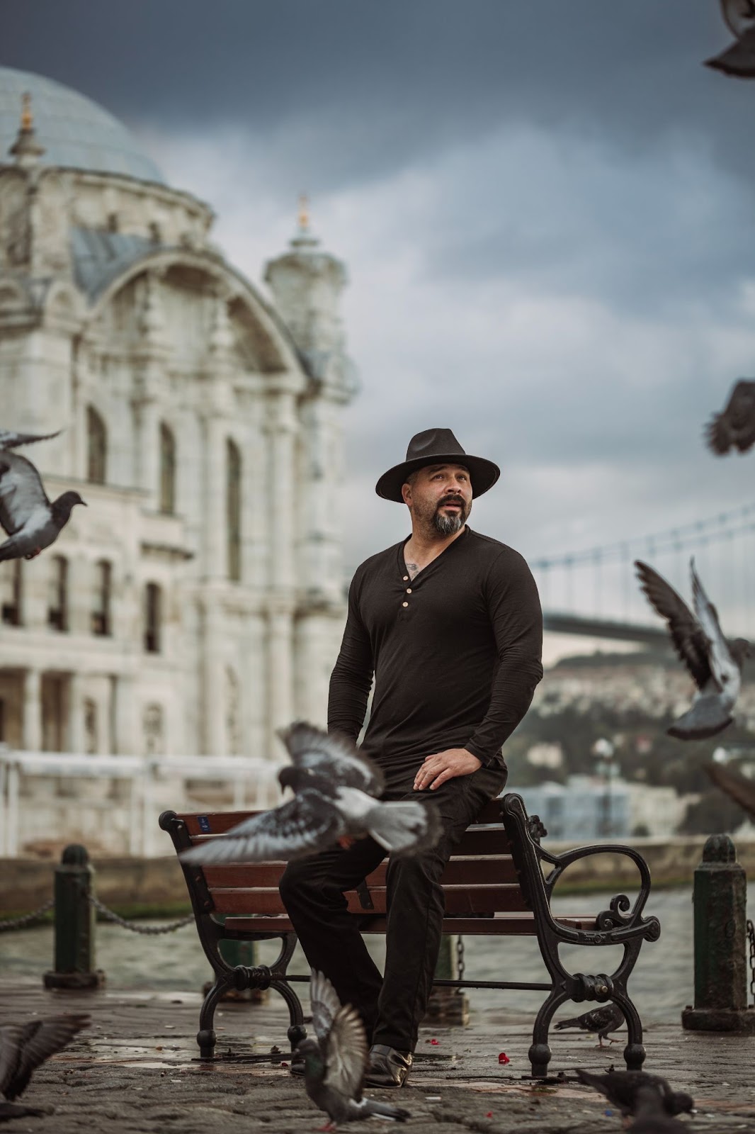 Rainy stroll by Ortaköy — pigeons rise, Bosphorus behind.