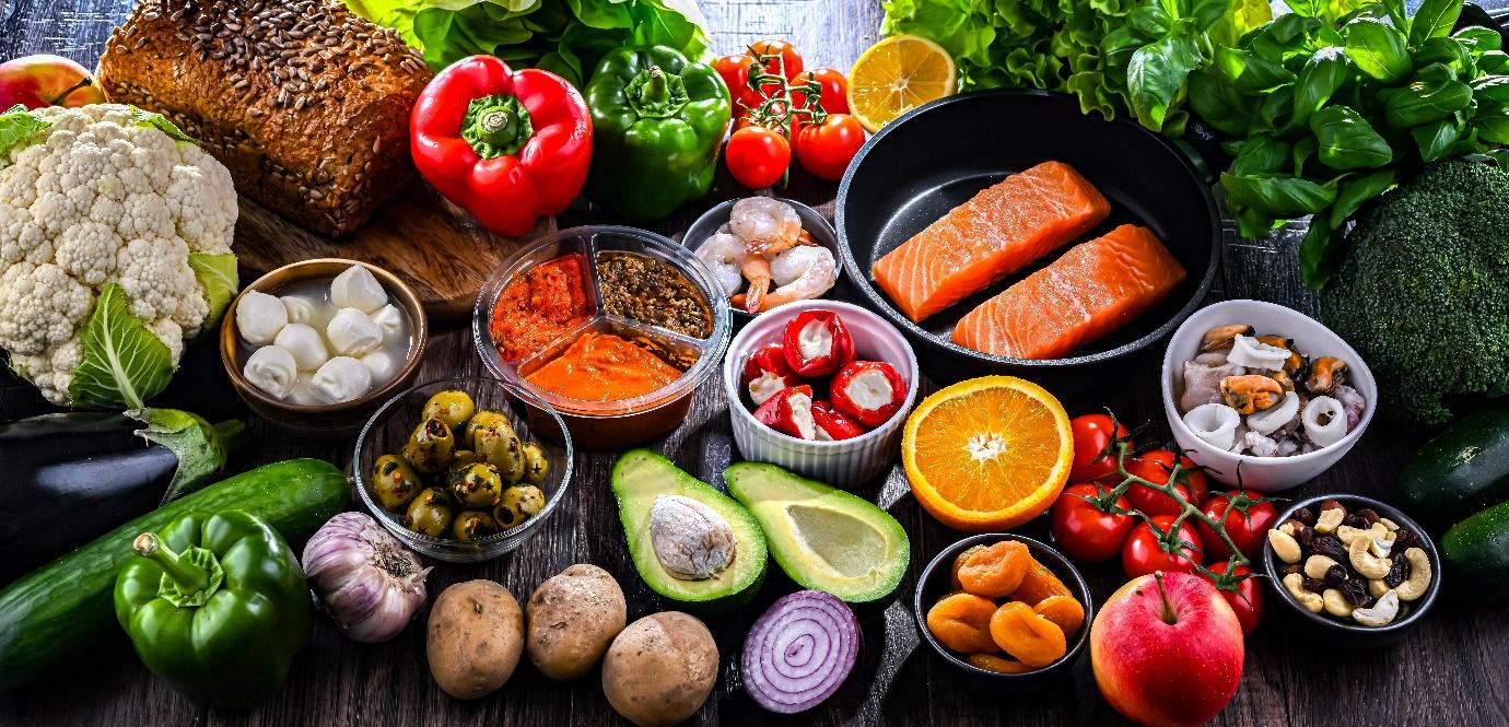 Alimentos frescos y saludables sobre una mesa: vegetales, frutas, salmón, frutos secos, pan integral y legumbres, ideales para una dieta equilibrada.