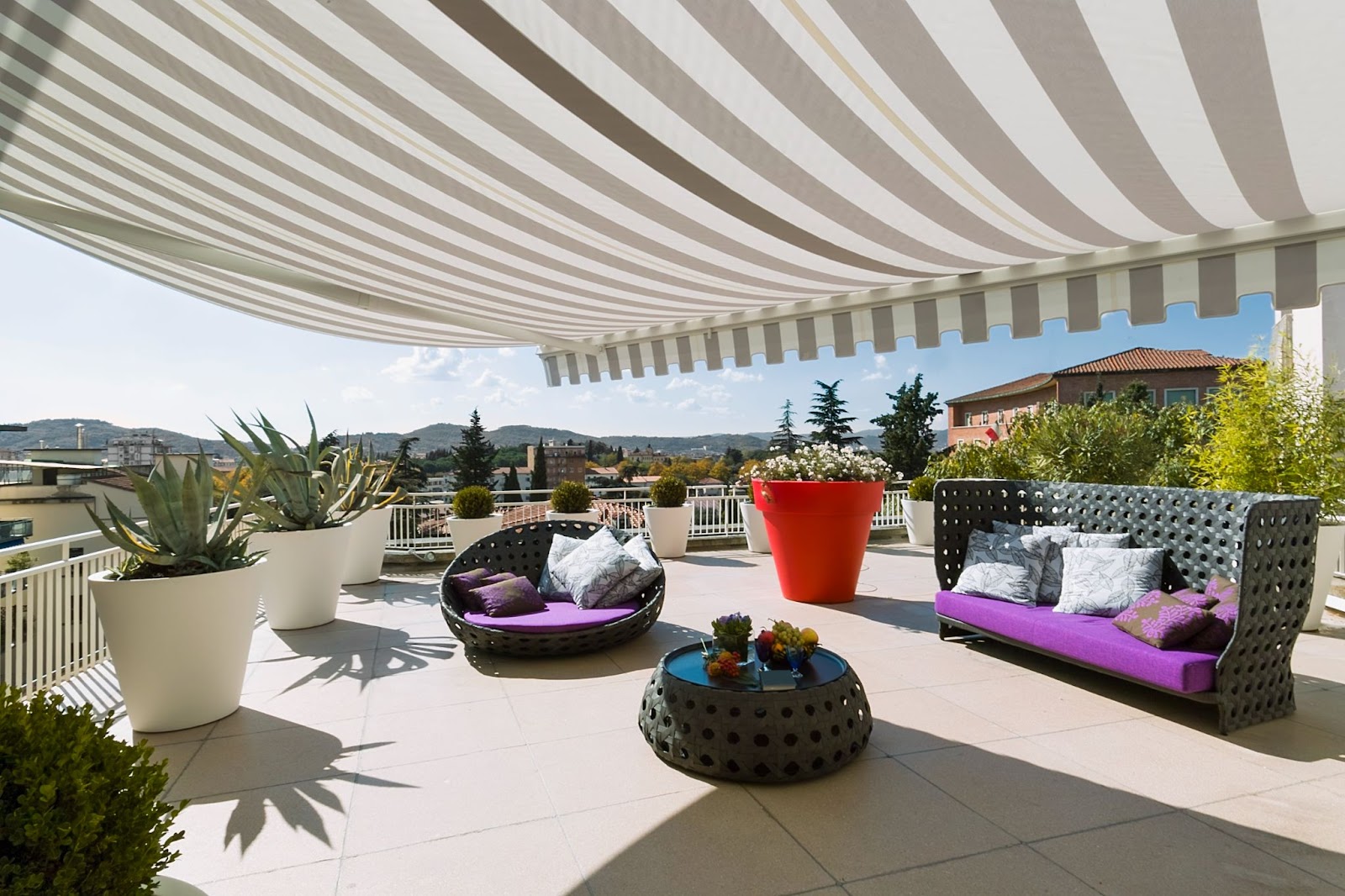 A modern terrace exterior with stylish furnishings beneath a striped awning, offering shade and a chic outdoor ambiance.