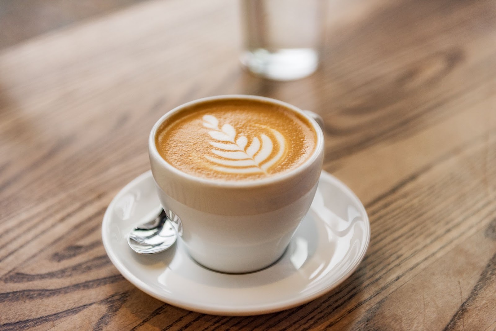 Šálka cappuccina s krásnym latte art na drevenom stole.