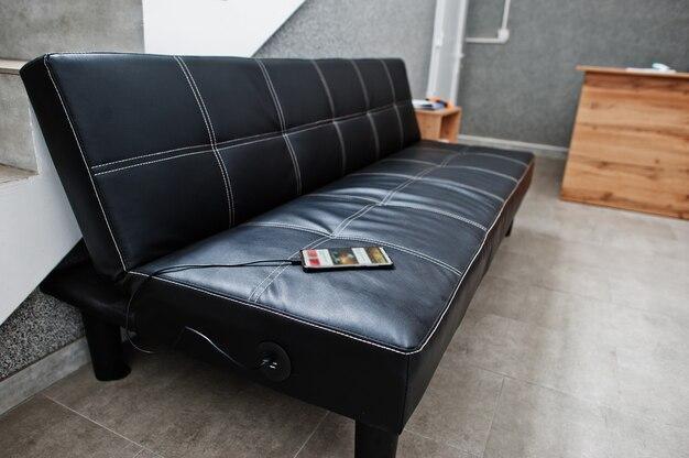 Outlet and USB Charger built into a black leather sofa charging mobile phone.