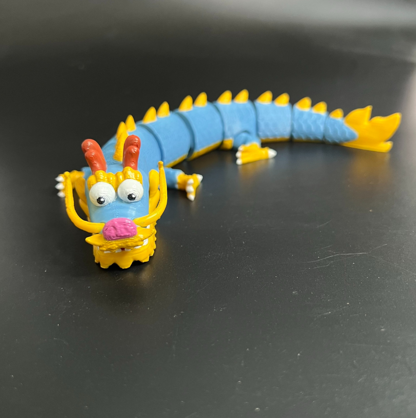 Cute articulated dragon 3D print model with blue segmented body, yellow spikes, and expressive cartoon face, STL available on PIXUP

