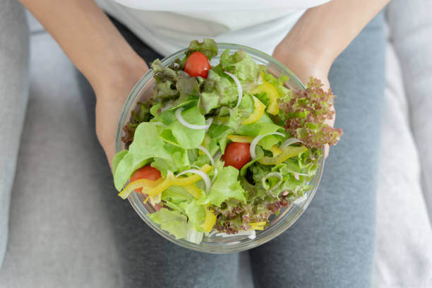 A person holding a bowl of fresh salad with leafy greens and vegetables, enjoying a light lunch for a midday detox.