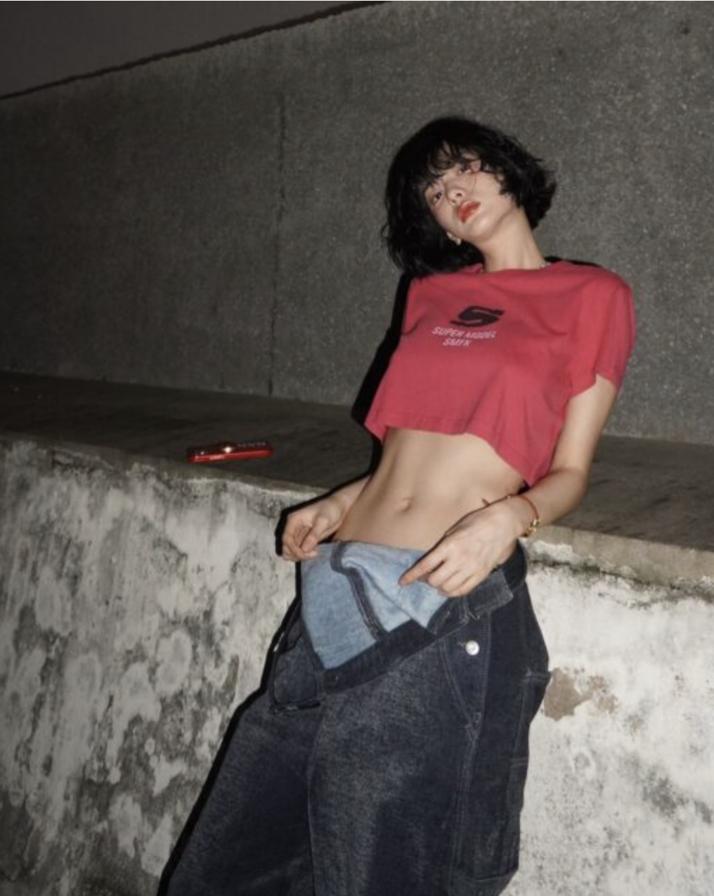 A picture ofNana on red top and black jean baggy resting on a wall