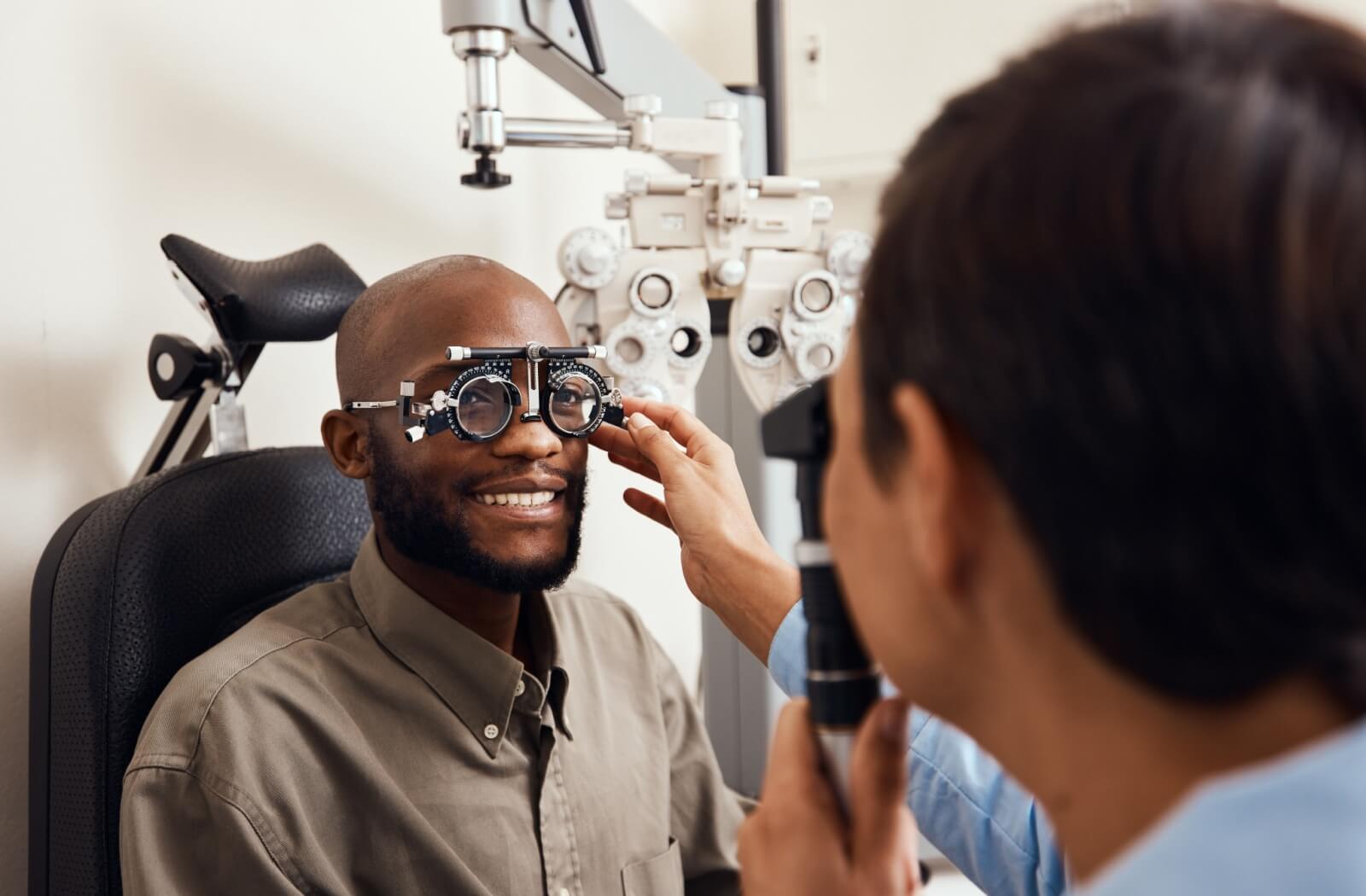 A patient wears a phoropter during an eye exam while the optometrist adjusts the lenses.