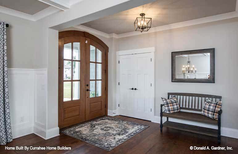 Foyer with a french front door, a distressed area rug, and a wooden bench topped with a framed mirror.