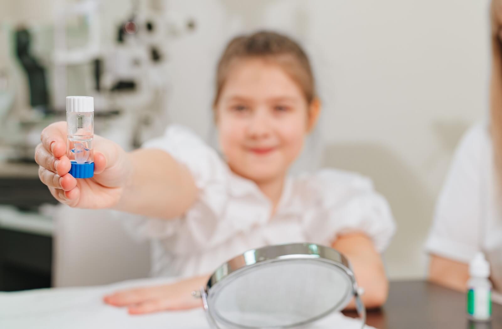 A young child proudly holds out their new Ortho-K prescription lenses after getting fitted at the optometrist