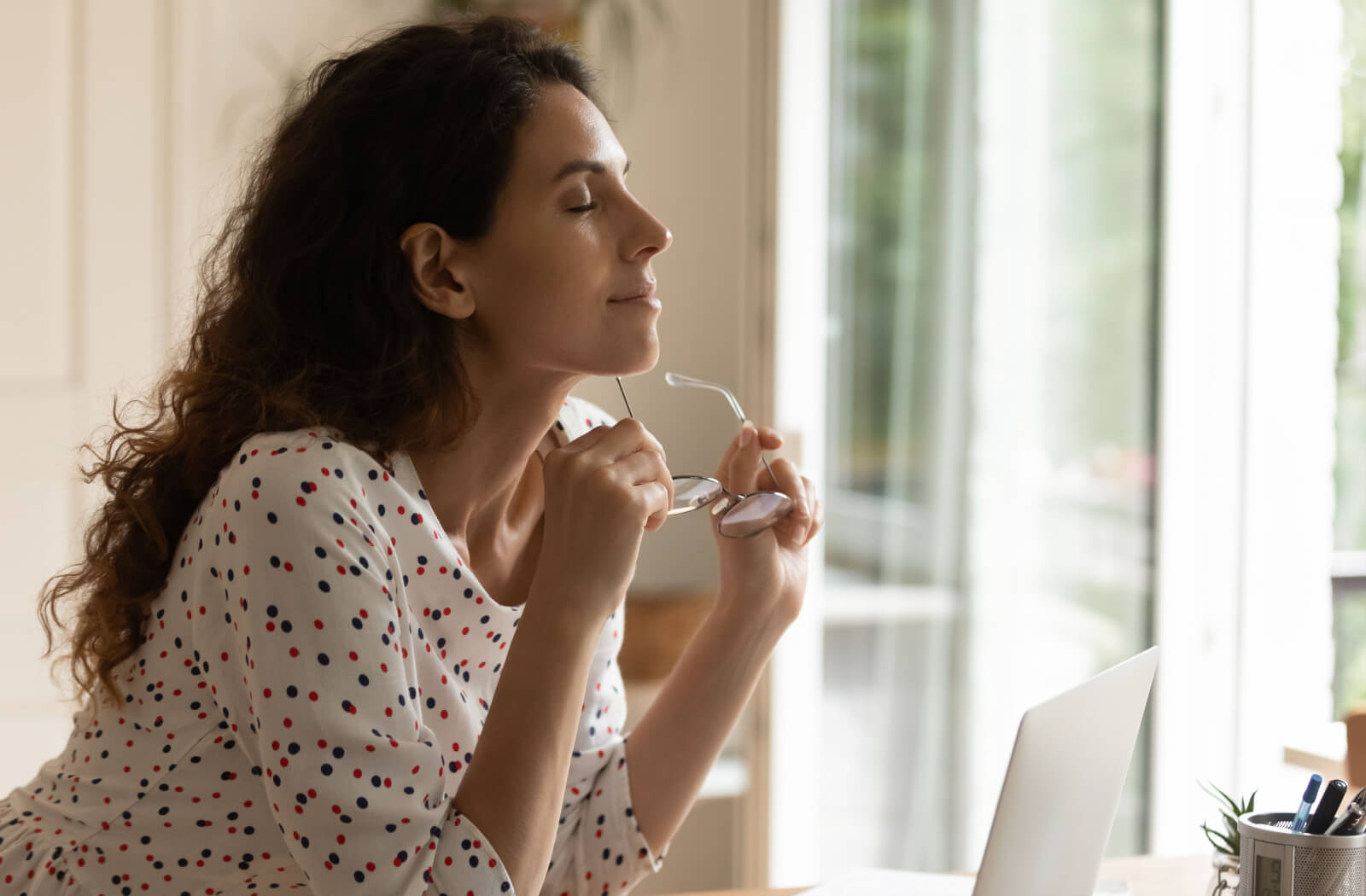 A young adult relaxing and taking off their glasses while working on a laptop to prevent digital eye strain.