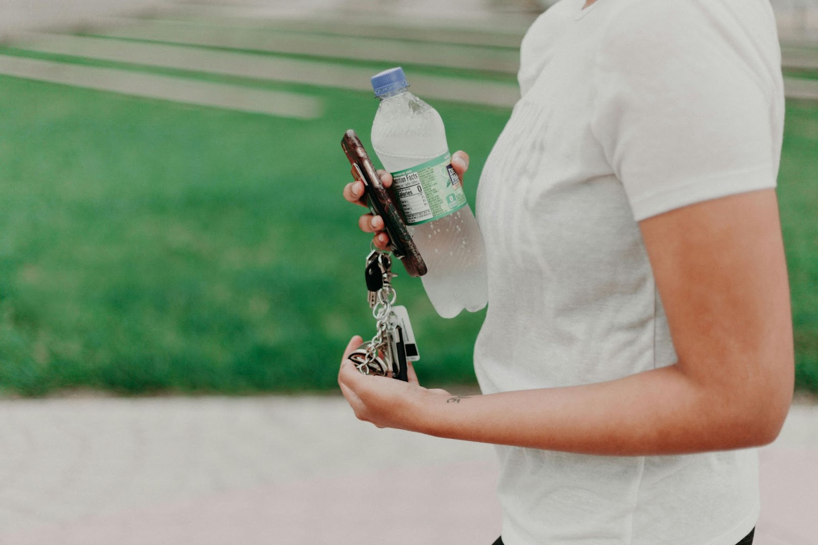 A man holding a bottle of water, a phone, and a bunch of keys