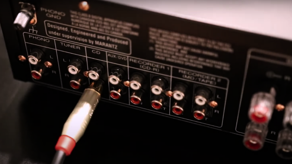 Rear view of a Marantz audio receiver with various input/output ports and an RCA cable plugged into the CD input.