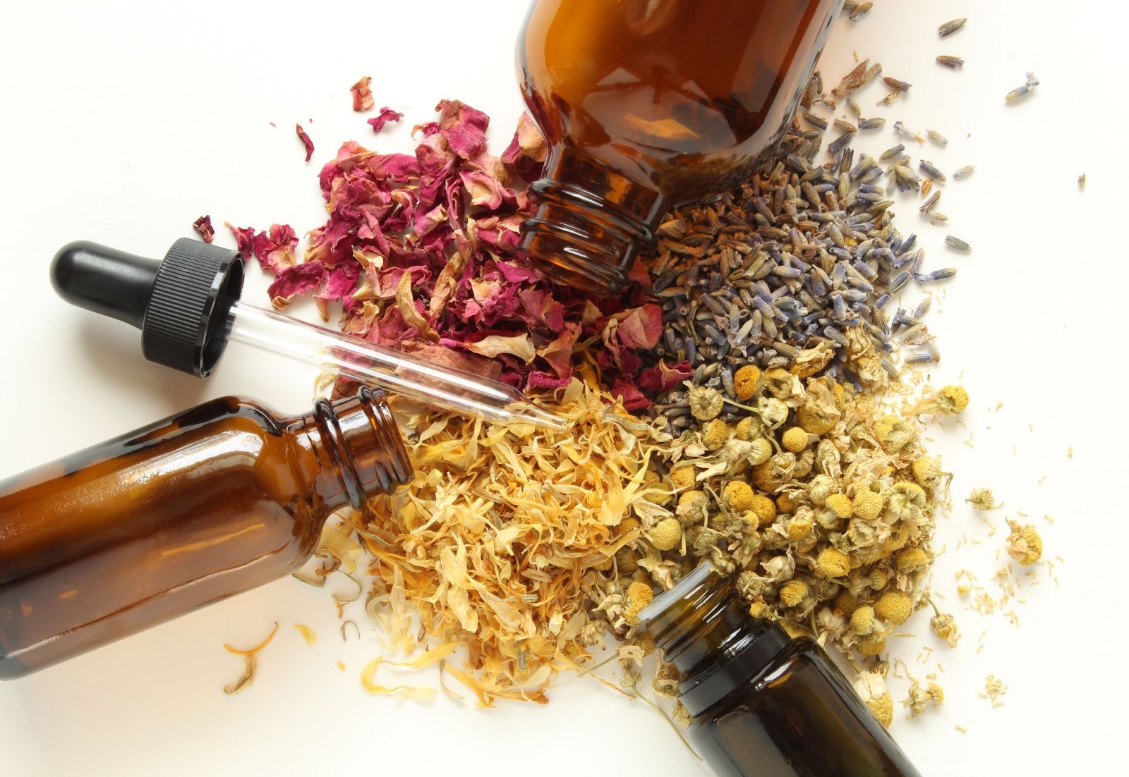 Amber bottles with a dropper placed over assorted herbs on a white background, representing herbal alternative medicine and natural healing remedies.