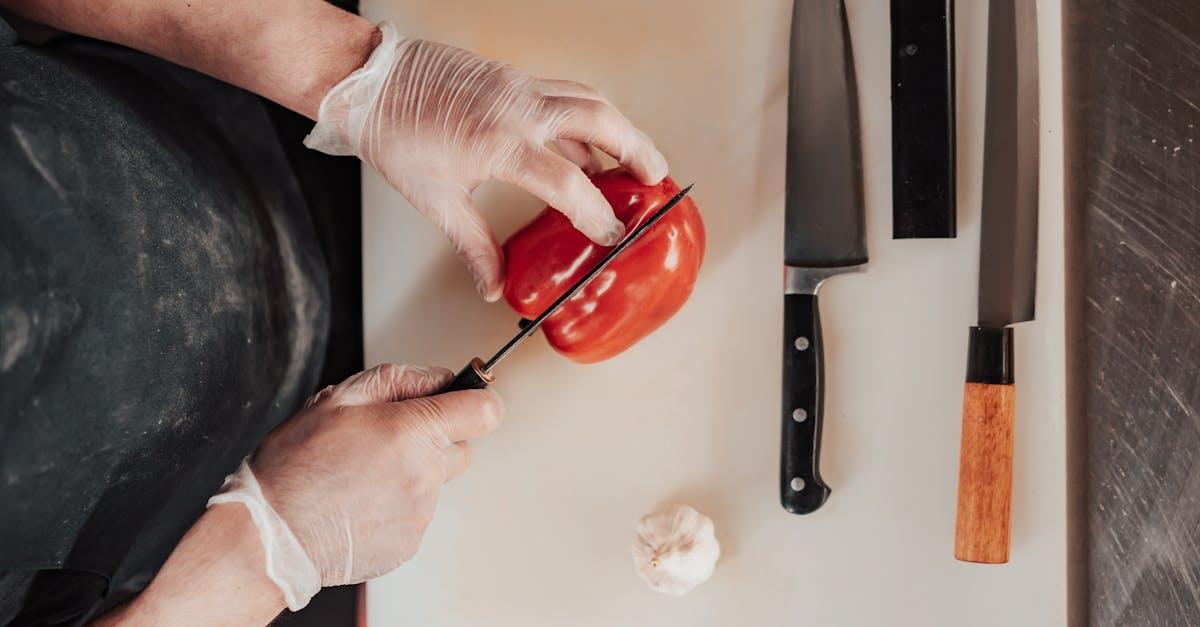 Top view of a chef slicing red pepper on a cutting board with knives, showcasing culinary skills.