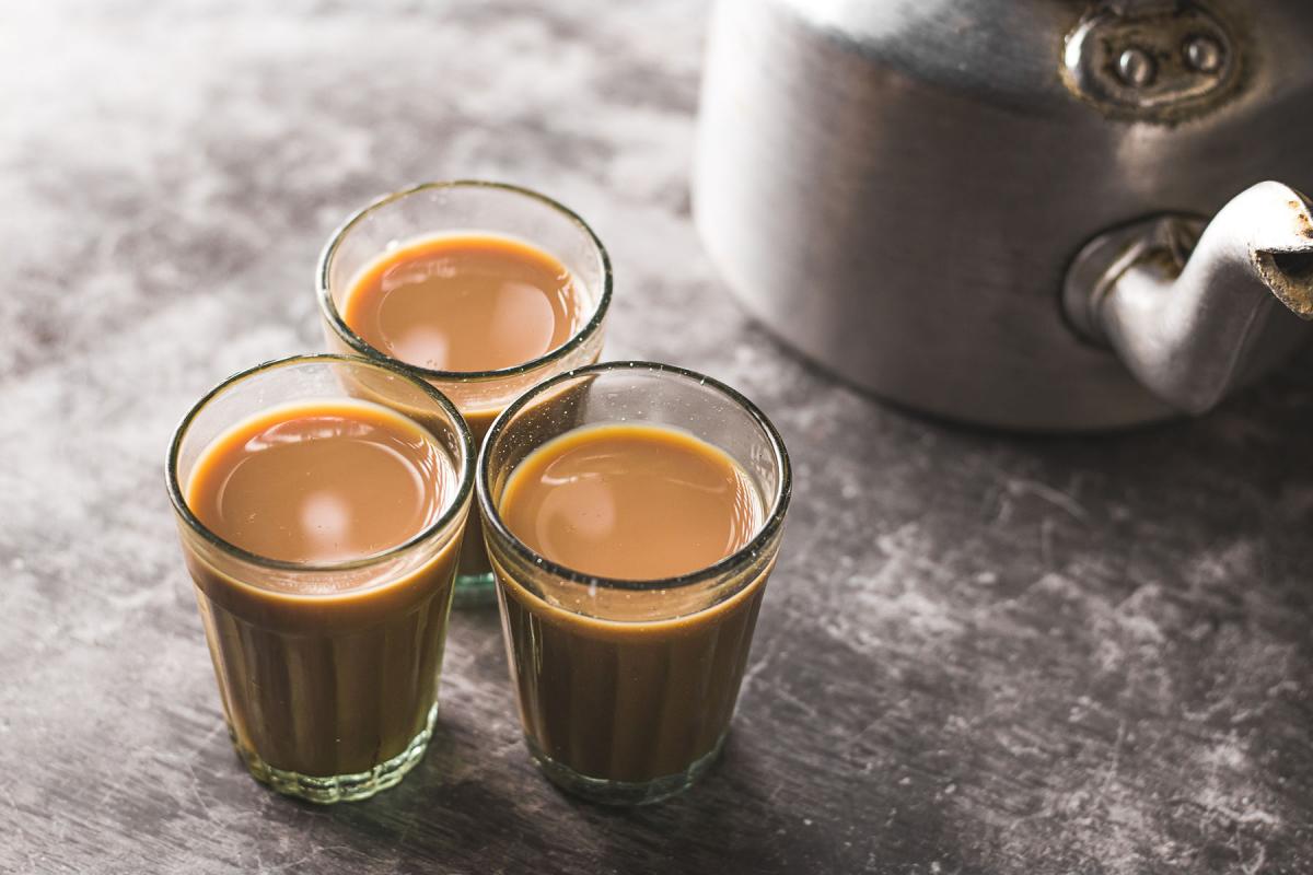 Three glasses of chai with a kettle in the background 