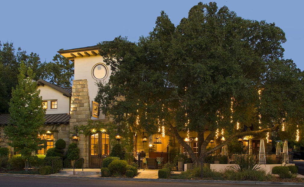 The charming exterior of Hotel Cheval in California, adorned with warm lights and nestled beneath a sprawling oak tree, epitomizing one of the top secret stays in California.