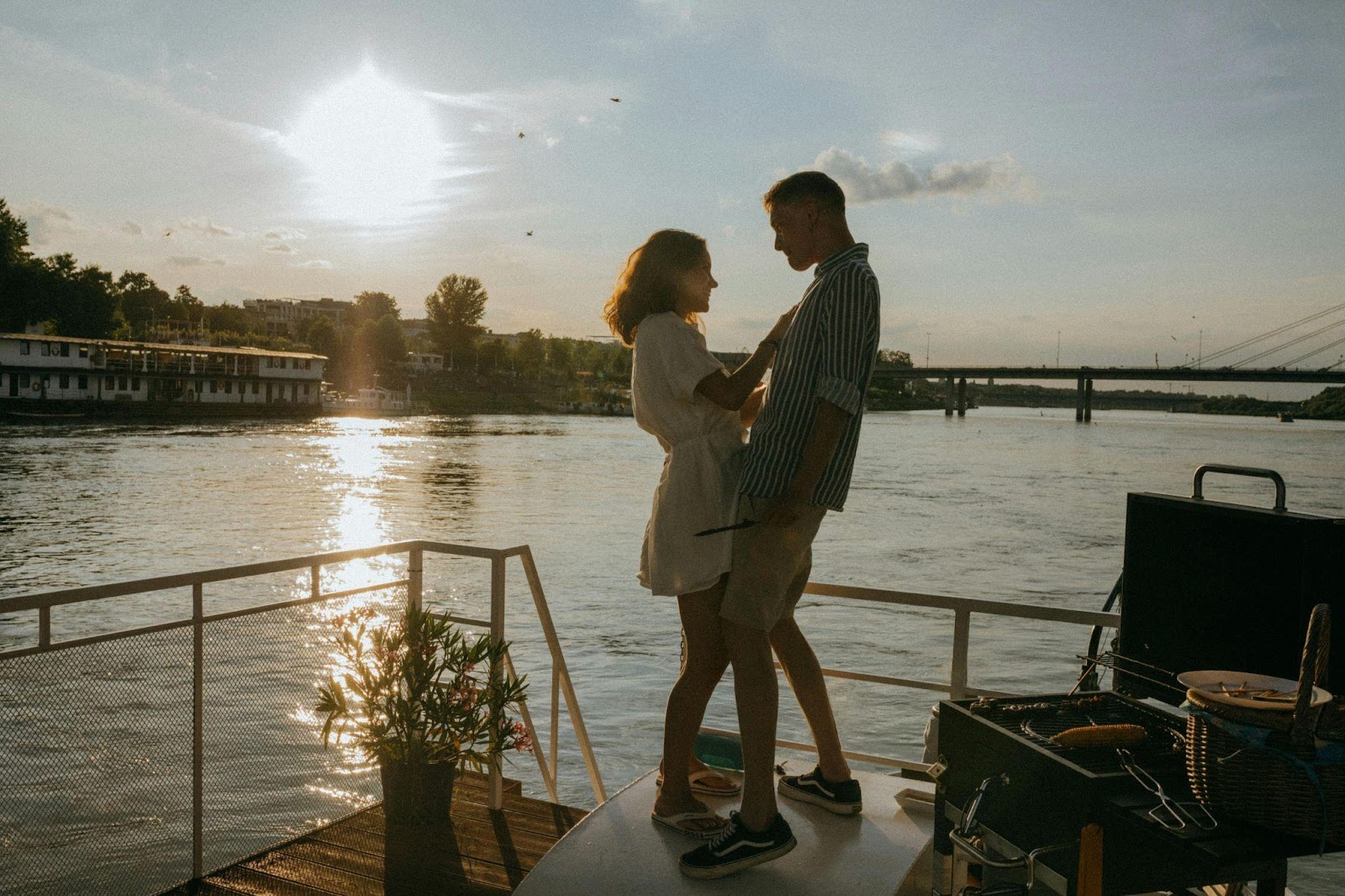 Romantic couple standing close together on the back deck of a boat during sunset, with a golden reflection on the water and a relaxed, intimate vibe.