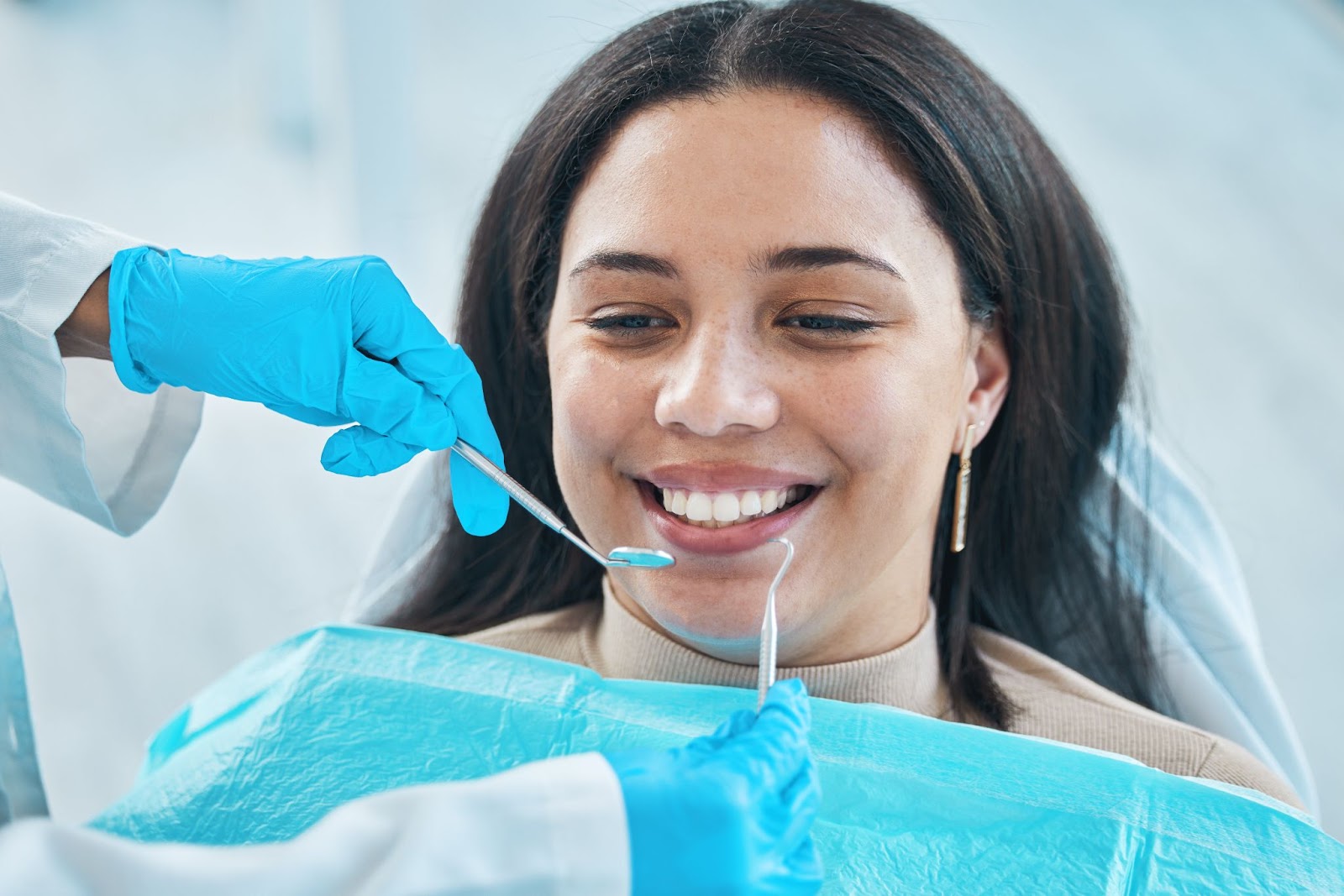 A dentist's hands holding metal dental tools during a teeth whitening procedure on a female patient.