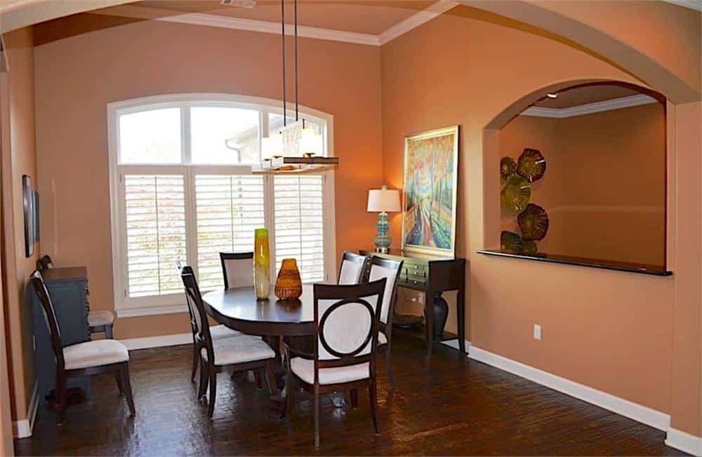 Formal dining room with louvered windows, an oval dining set, and a dark wood console table topped with a painting and a table lamp.