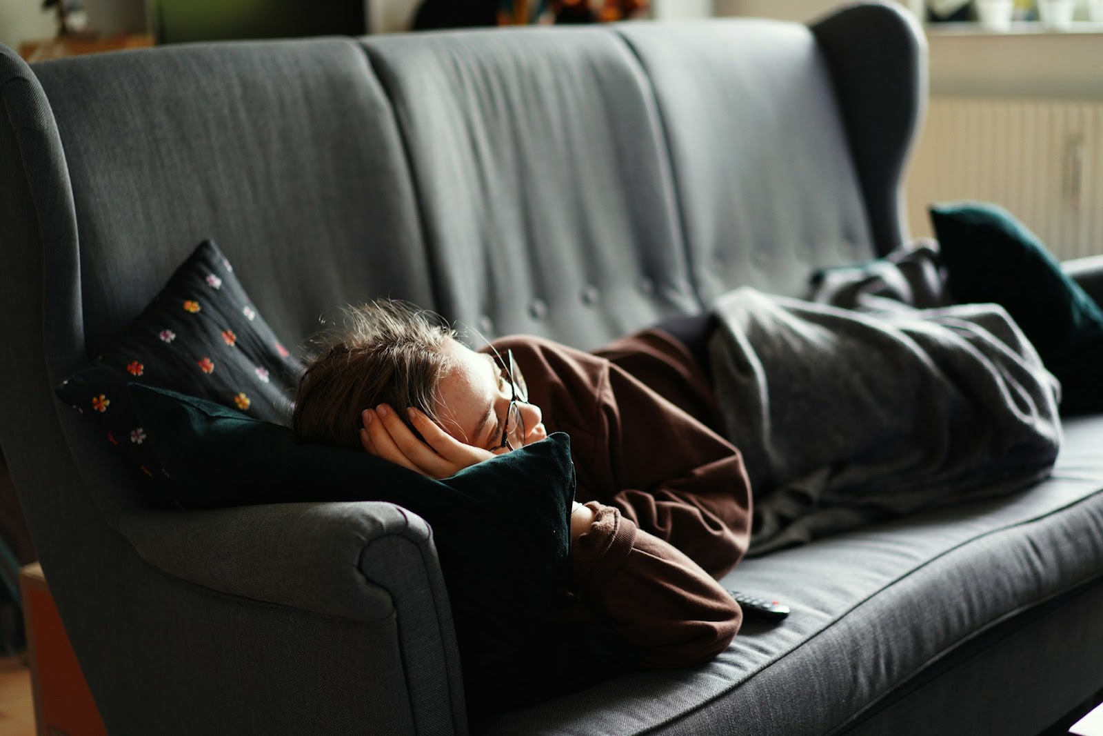 A woman peacefully sleeping on a cozy couch, wrapped in a soft blanket, enjoying a moment of relaxation.